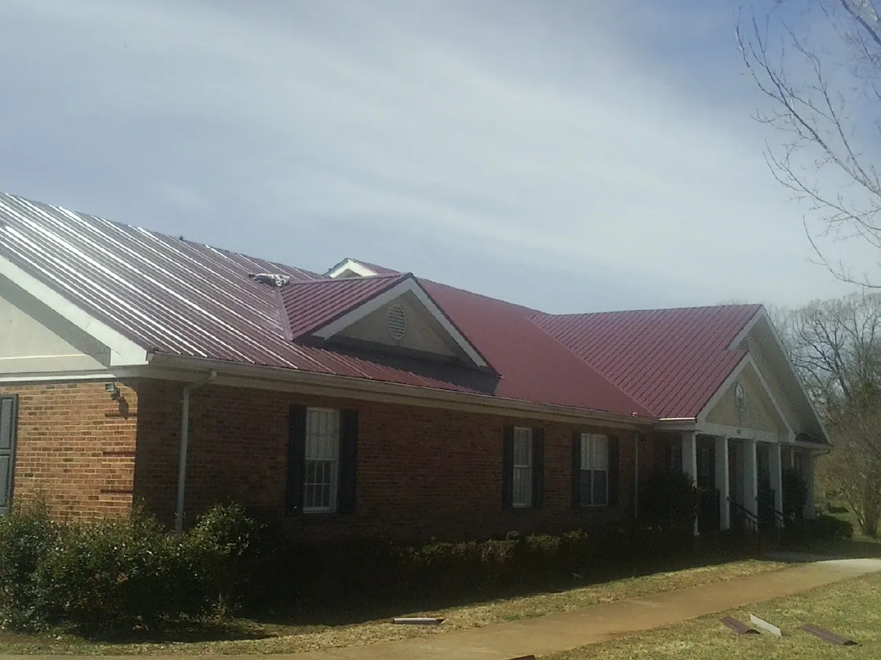 Red metal roof with gabled entries on a long brick building, from a Hail Damage Roof Repair job in Dickey