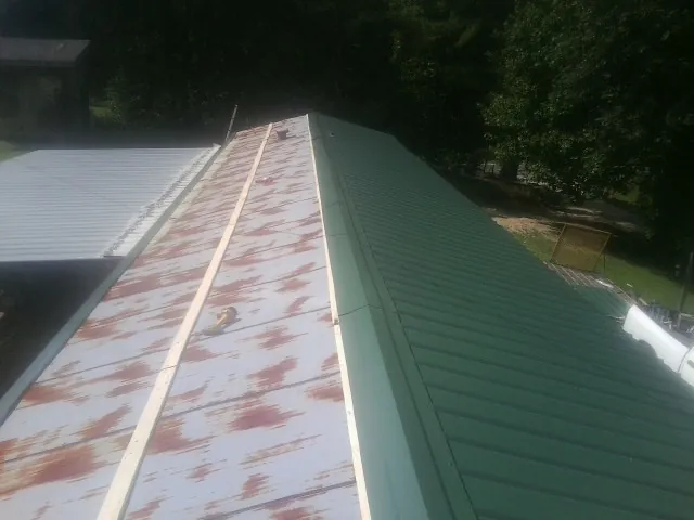 Old rusted panels beside newly installed green metal roofing — Wind Damage Roof Repair by Roofing Brothers in Dickey