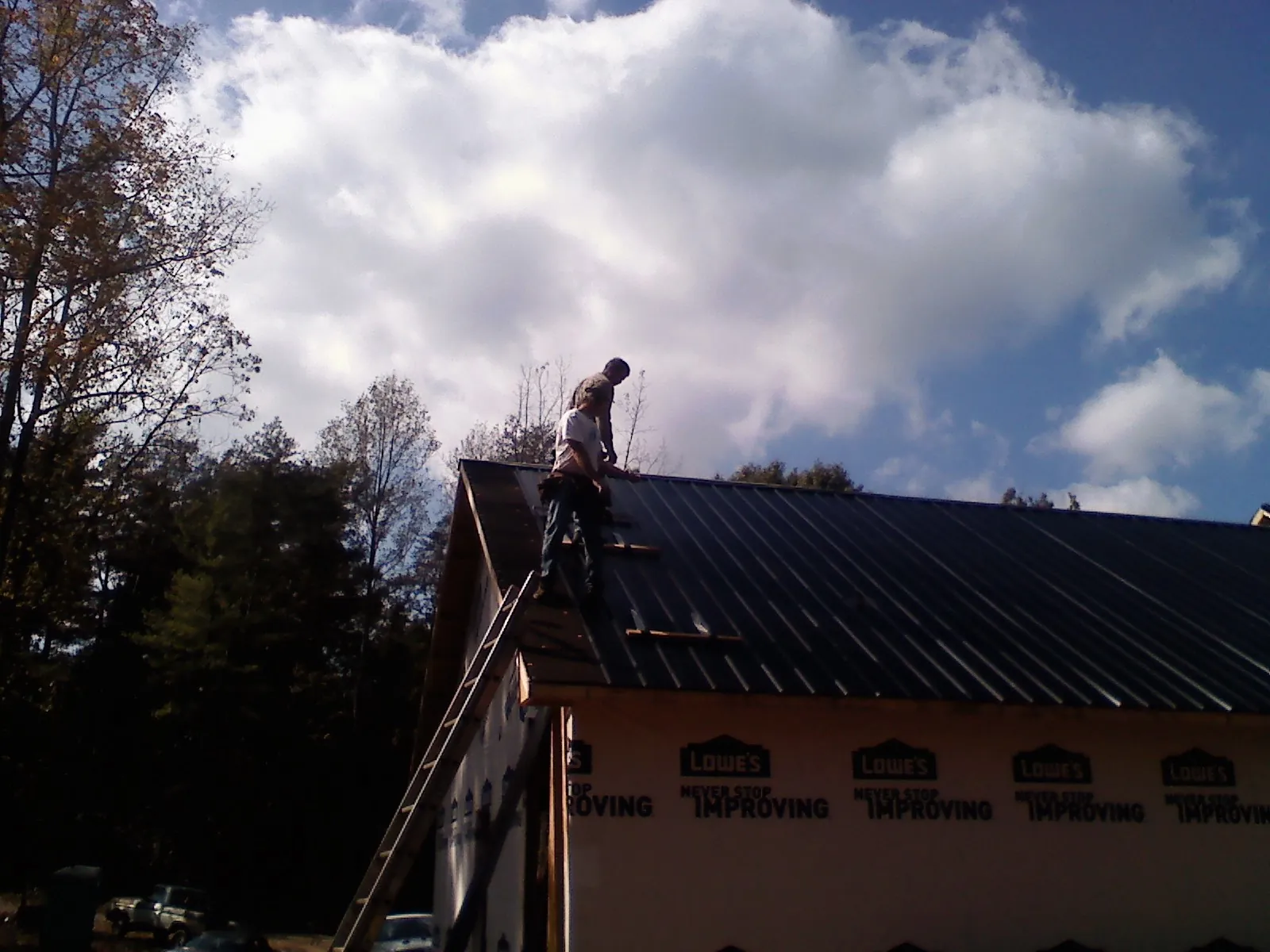 Roofer fastening dark metal panels high against a cloudy sky, from a Roof Inspection job in Dickey