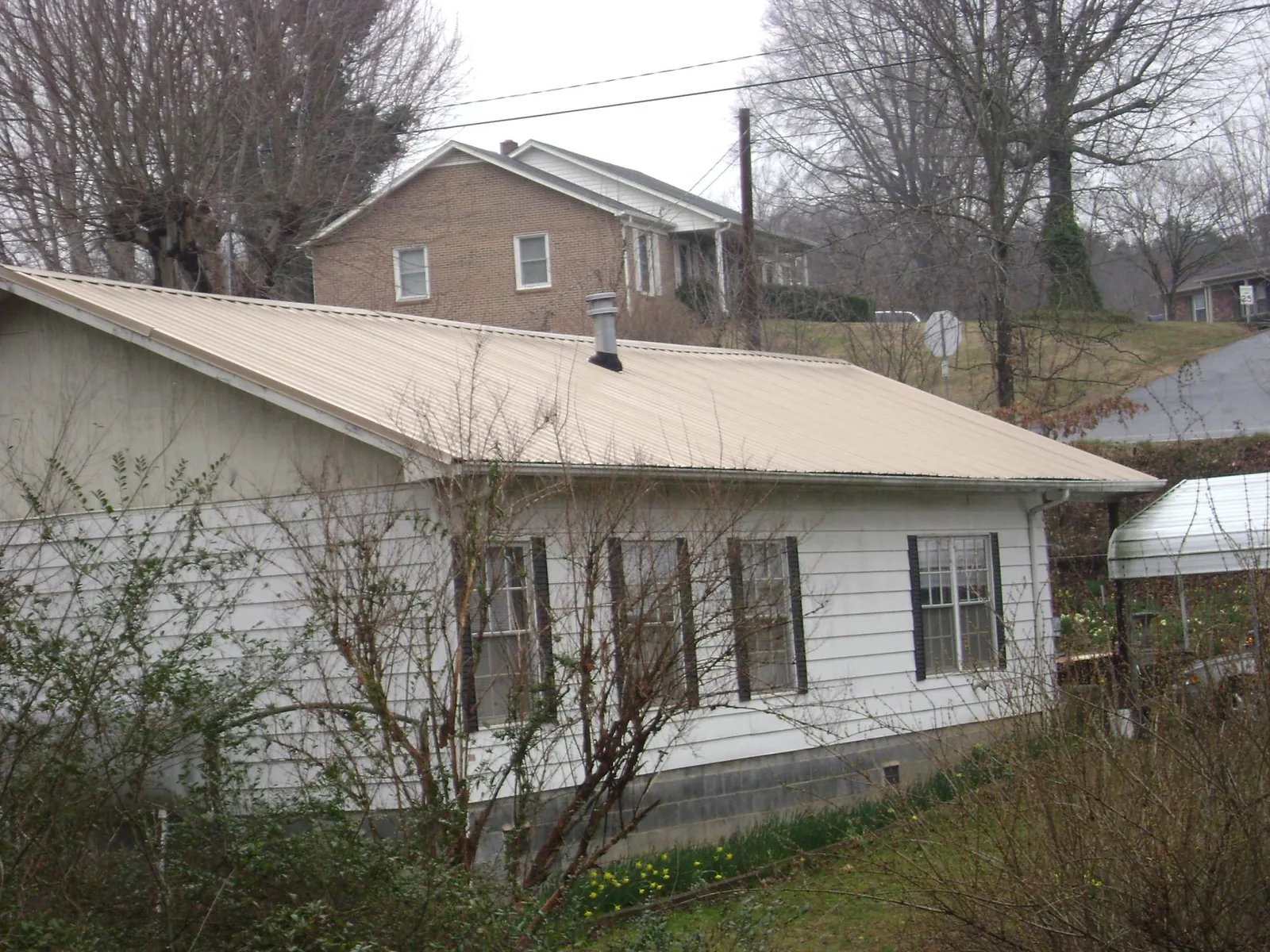 Tan metal roof on a white sided house set into a hillside — Commercial Roofing by Roofing Brothers in Dickey